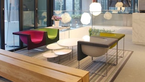 A modern interior with a reception desk, colorful chairs, and a long wooden bench. - STAY B Hotel Myeongdong (Seoul)