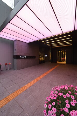 A hotel entrance with a modern design, including a reception desk, a sign reading "STAYB", and a pathway leading to the entrance.