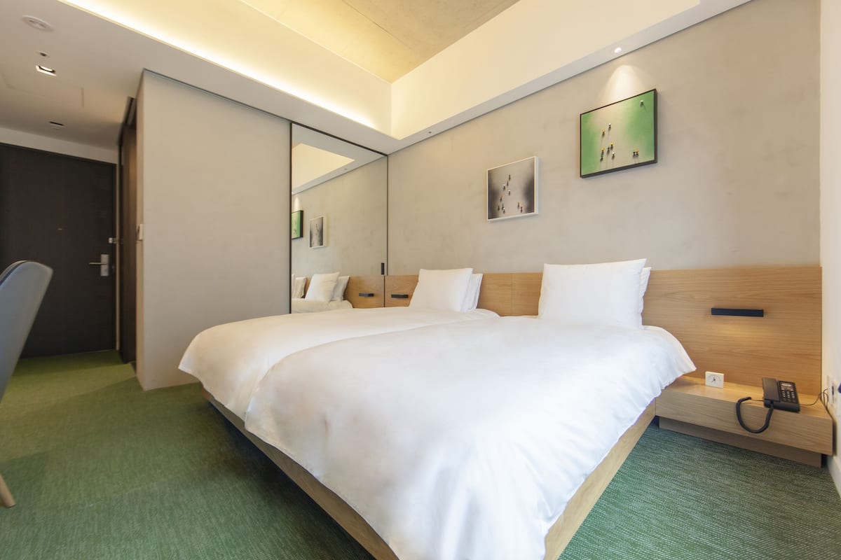 Ett modernt hotellrum med en stor säng, ett nattduksbord med en telefon, en liten väckarklocka och en grön matta.