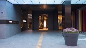 A hotel entrance with a large planter of flowers, a visible sign for 'STAYB', and a 'HAZ' sign. - STAY B Hotel Myeongdong (Seoul)