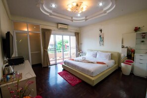 Una habitación de hotel con cama, escritorio, televisión y balcón con cortinas.