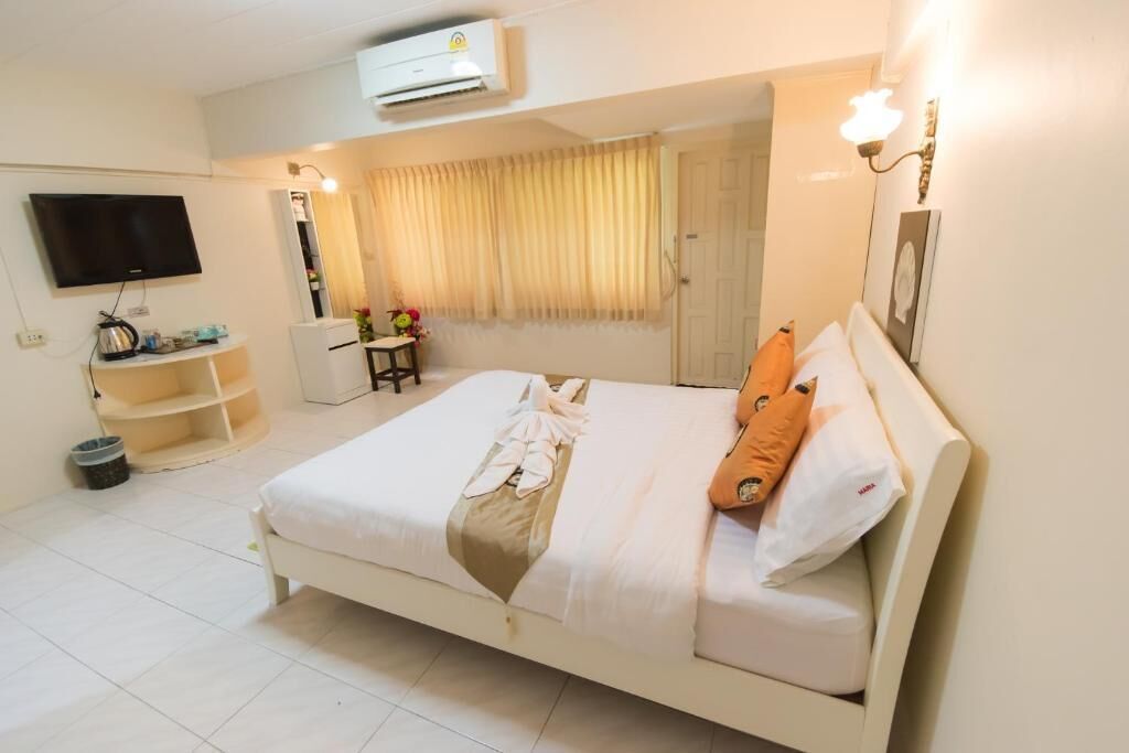 Une chambre d’hôtel bien rangée, avec un lit, une télévision, une petite table sur laquelle est posé un vase, et une armoire.