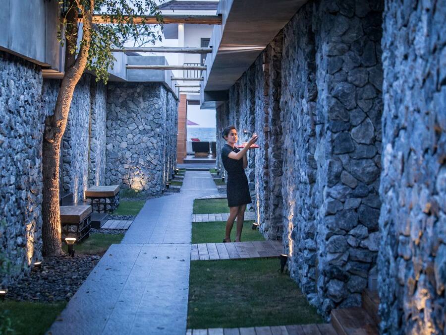 A stone-walled corridor with a pathway, benches, and a person taking a photo.