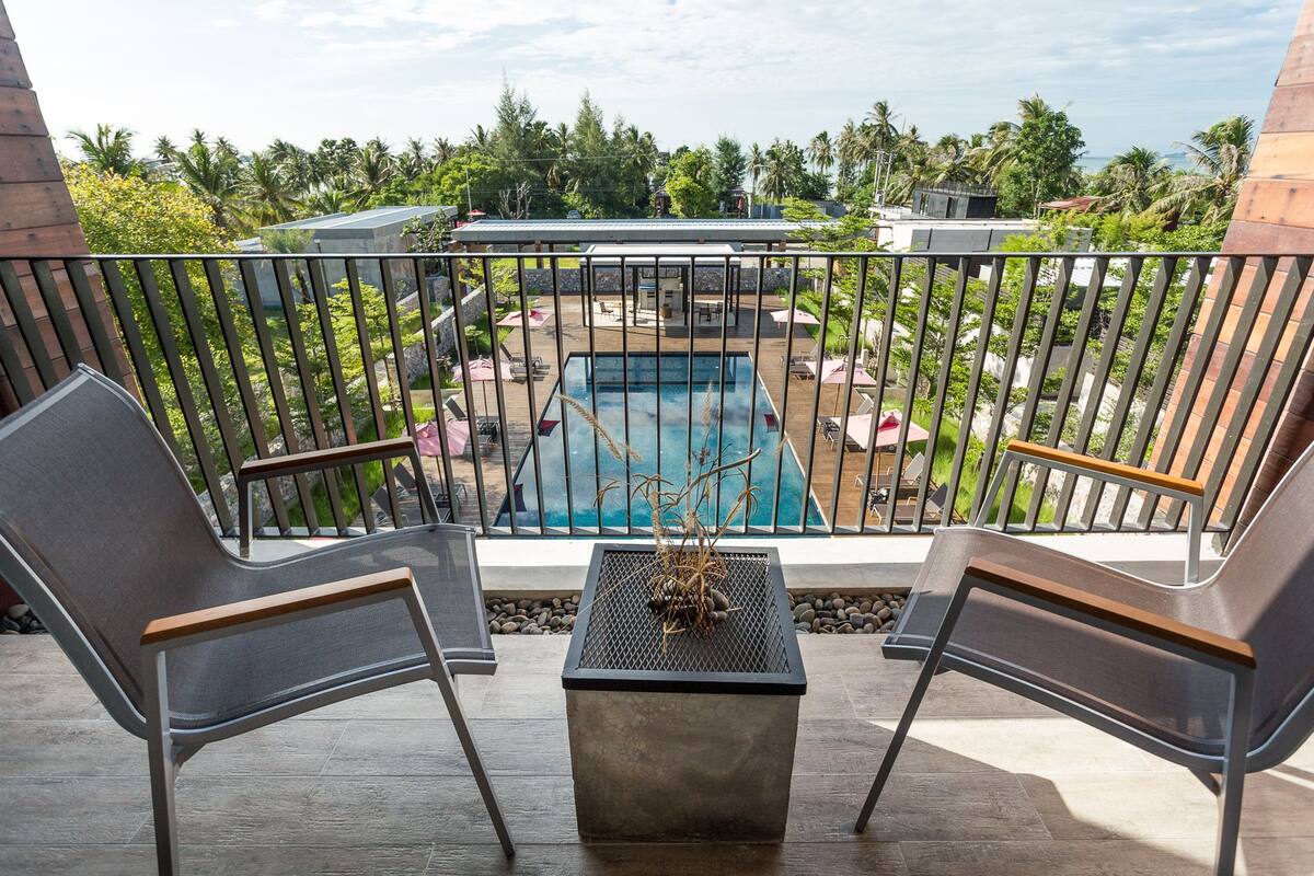 A balcony with two chairs, a small table, and a view of a pool area with umbrellas and lounge chairs.
