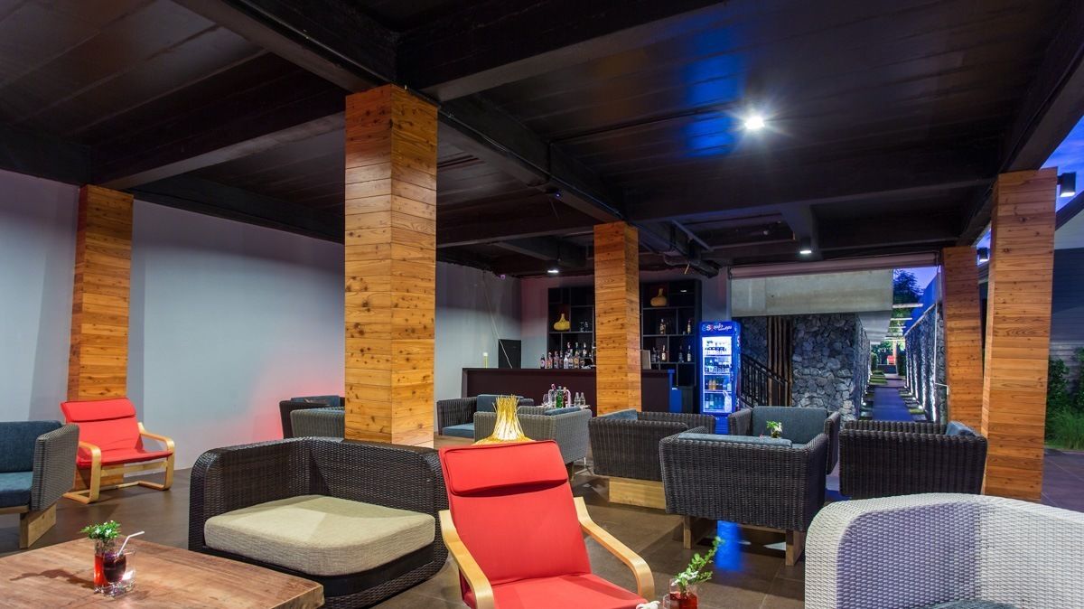 A modern lounge area with wicker furniture, wooden pillars, and a bar area with bottles and a menu display.