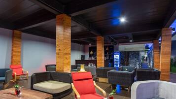 A modern lounge area with wicker furniture, wooden pillars, and a bar area with bottles and a menu display.