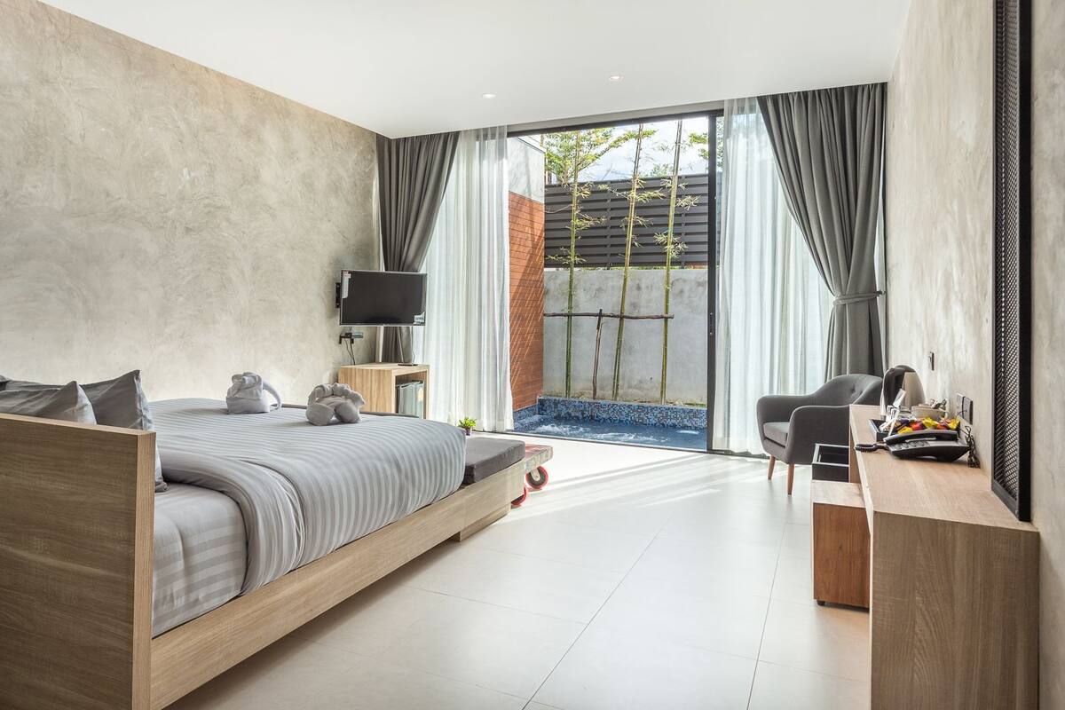 A modern bedroom with a wooden bed, a desk, and a view of a bamboo garden.