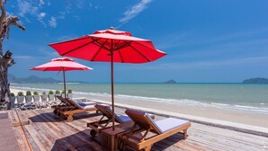 A wooden deck with lounge chairs and red umbrellas overlooking a beach. - Lipda Resort (Prachuap Khiri Khan)