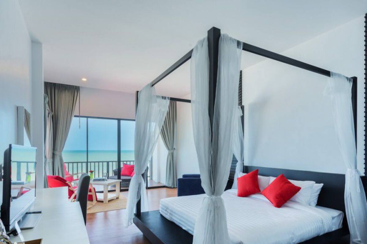 A modern hotel room with a four-poster bed, a balcony with a view, and a desk with a chair.