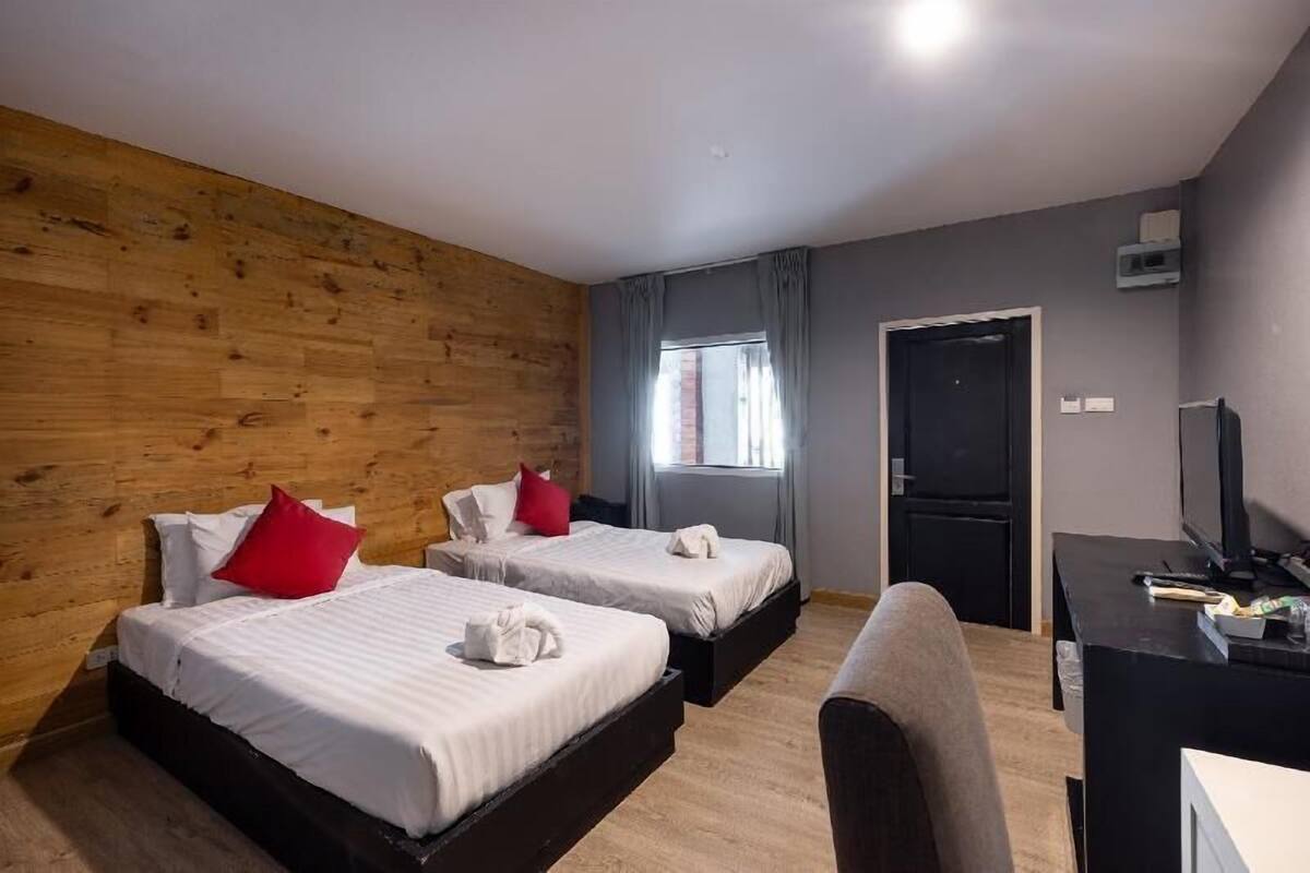 A hotel room with two beds, a desk, a television, and a window with curtains.