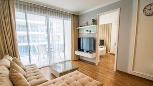 Una sala de estar moderna con un sofá, un televisor montado en la pared y una zona de comedor visible a través de un panel de vidrio.
