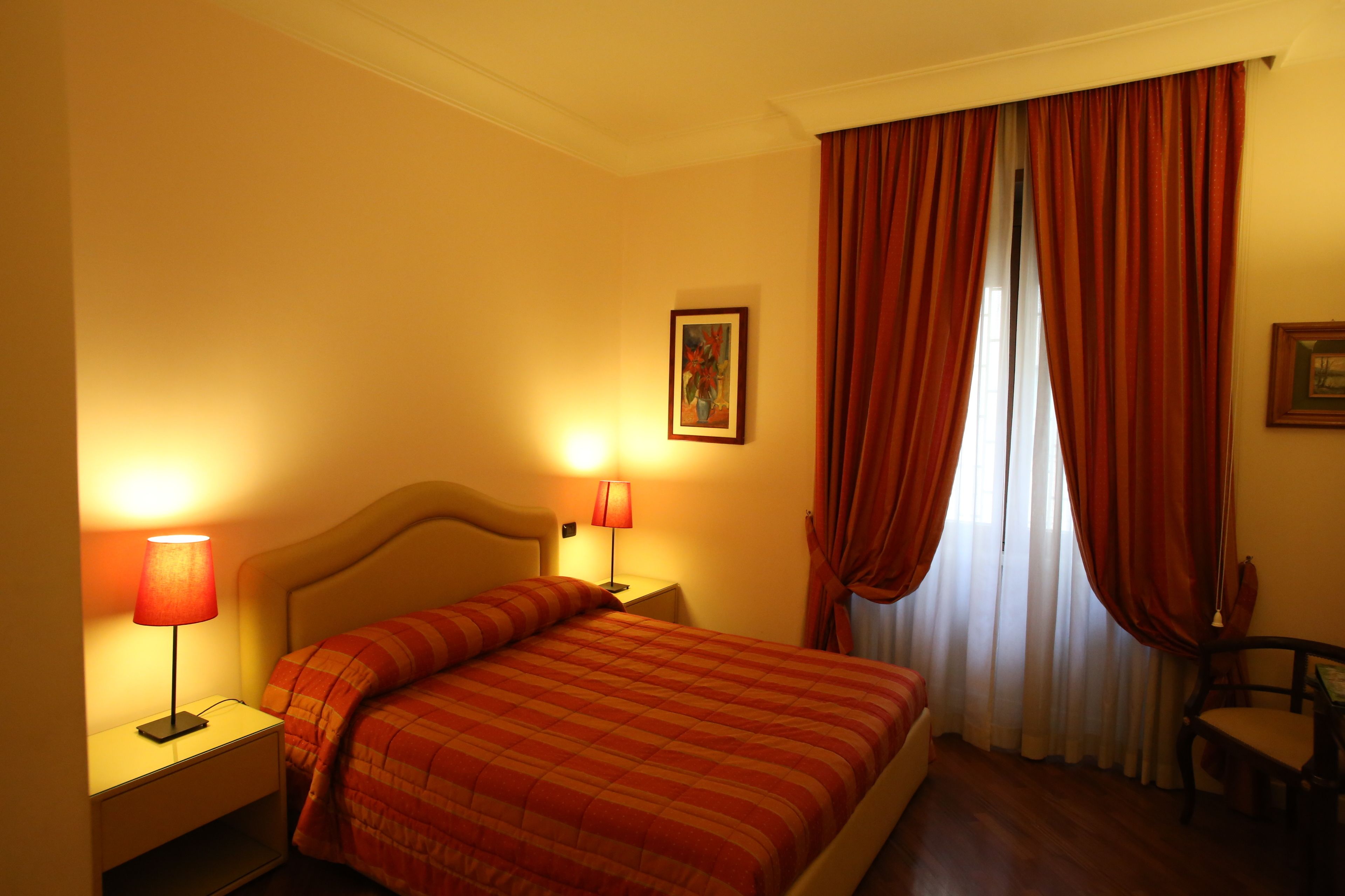 A hotel room with a bed, two bedside lamps, a chair, and a window with curtains.