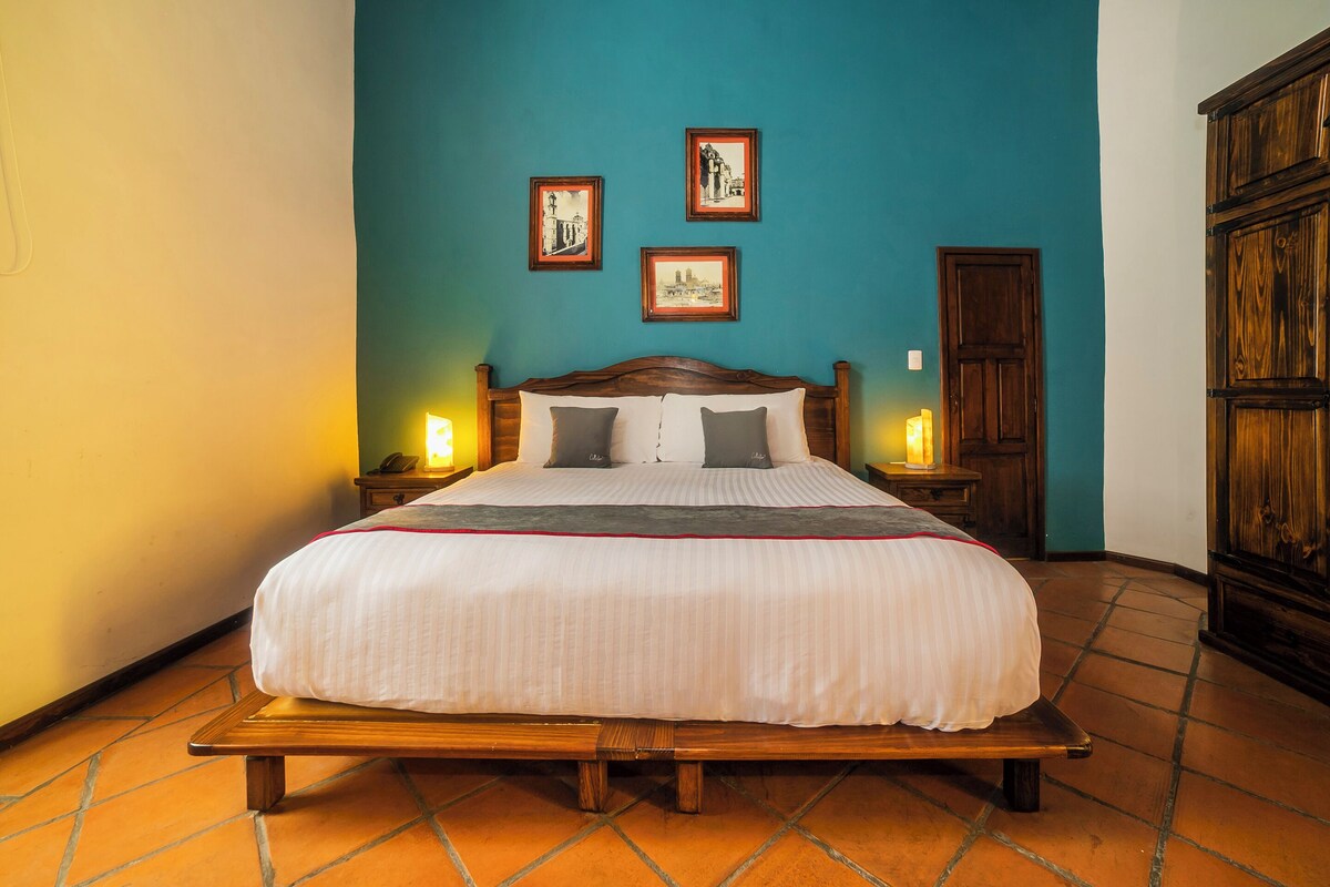 Una cama con estructura de madera, cabecera y cubrecama blanco. Hay dos mesitas de noche con lámparas.