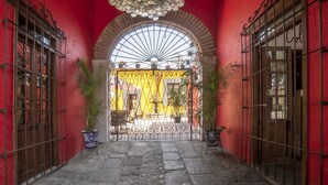 Un pasillo con paredes rojas, un gran arco de entrada, puertas de metal y una lámpara colgante.