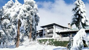 A modern hotel with a flat roof and large windows, surrounded by snow-covered trees. - Hotel Bor (Samokov)