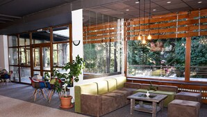 A modern lounge area with a sofa, chairs, a table, and a large window offering a view of trees. - Hotel Bor (Samokov)
