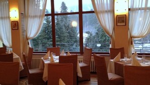 A restaurant with tables set for dining, large windows with curtains, and a view of trees outside. - Hotel Bor (Samokov)