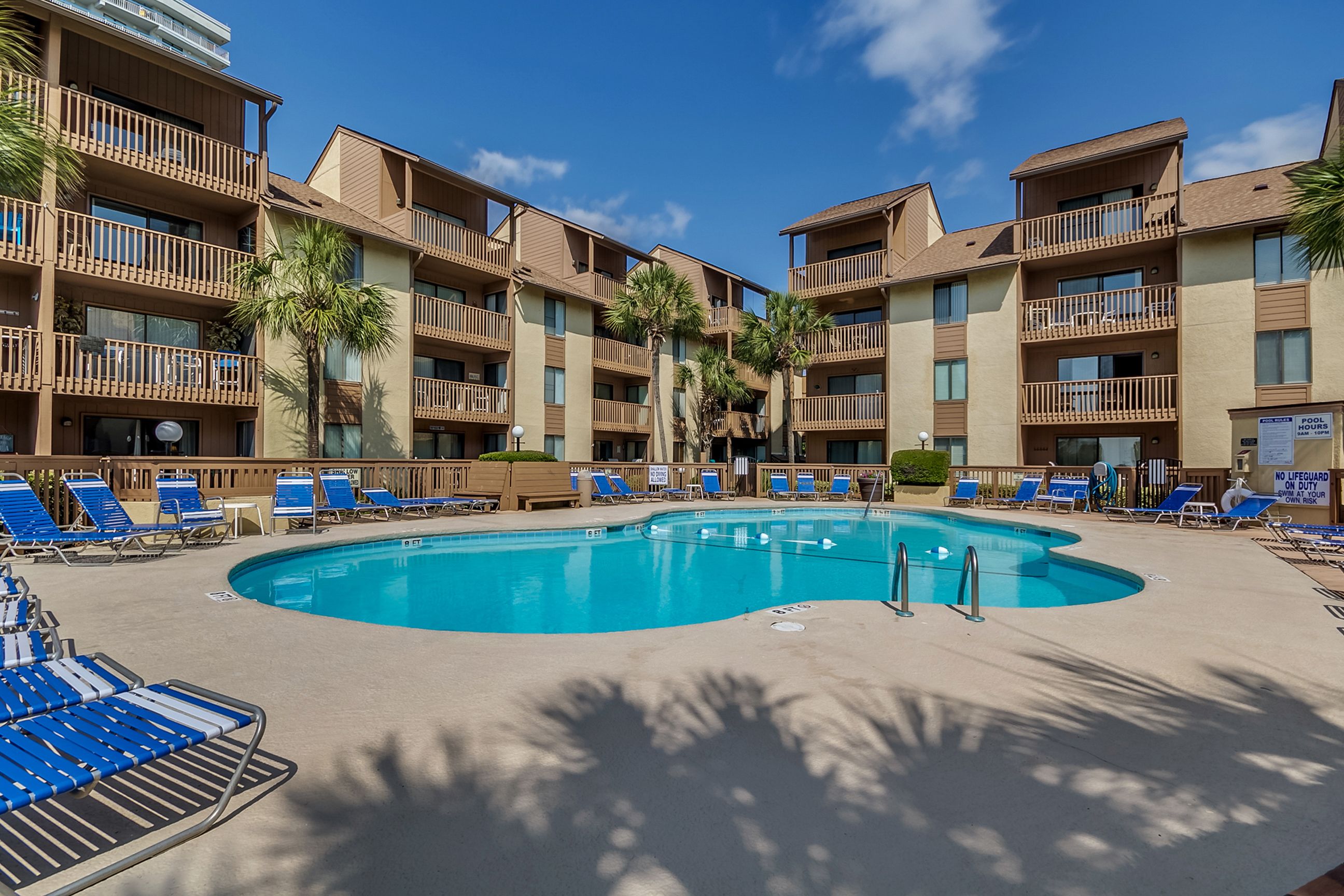 A hotel with multiple balconies, a swimming pool, and sun loungers.