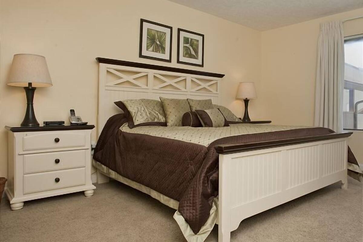 A bedroom with a bed, two bedside tables, a nightstand, a dresser, and two framed pictures on the wall.