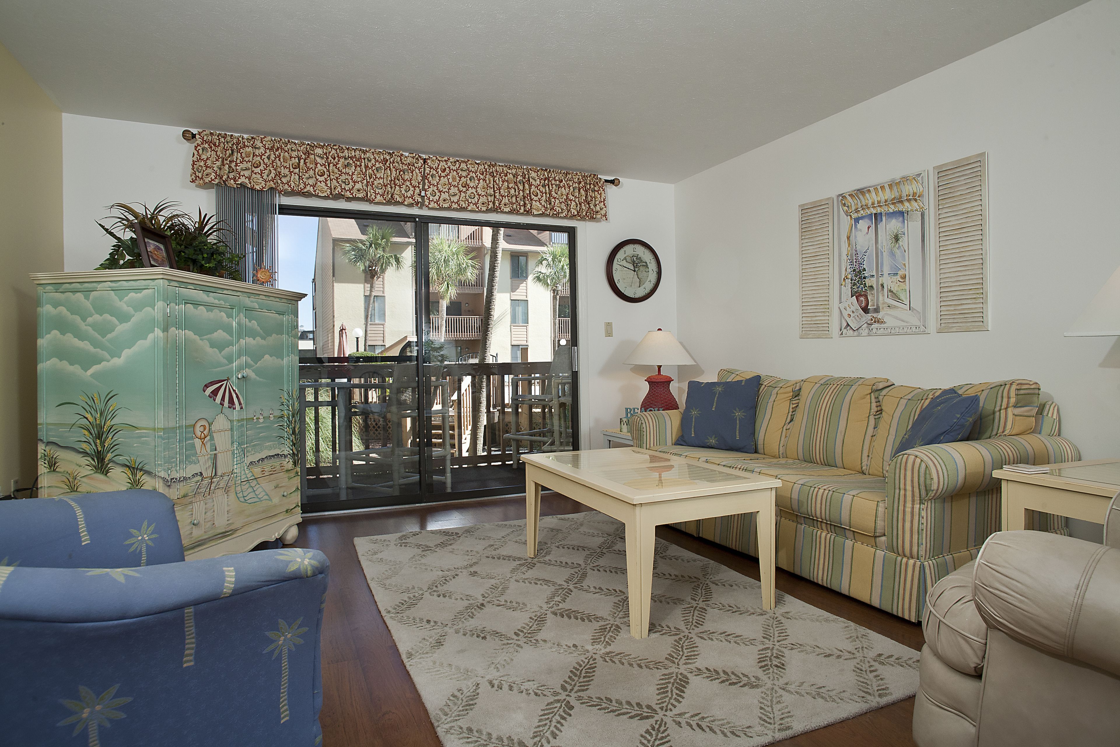 A living room with a sofa, armchair, coffee table, and a cabinet with a beach mural.