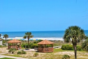 A beach view with two wooden gazebos, a palm tree, and the ocean in the background. - Anchorage I (Myrtle Beach)