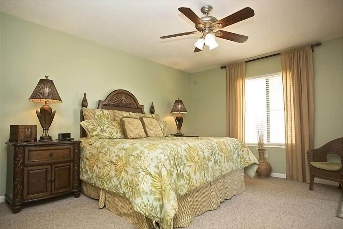 A bedroom with a bed, two nightstands, a ceiling fan, and a window with curtains.