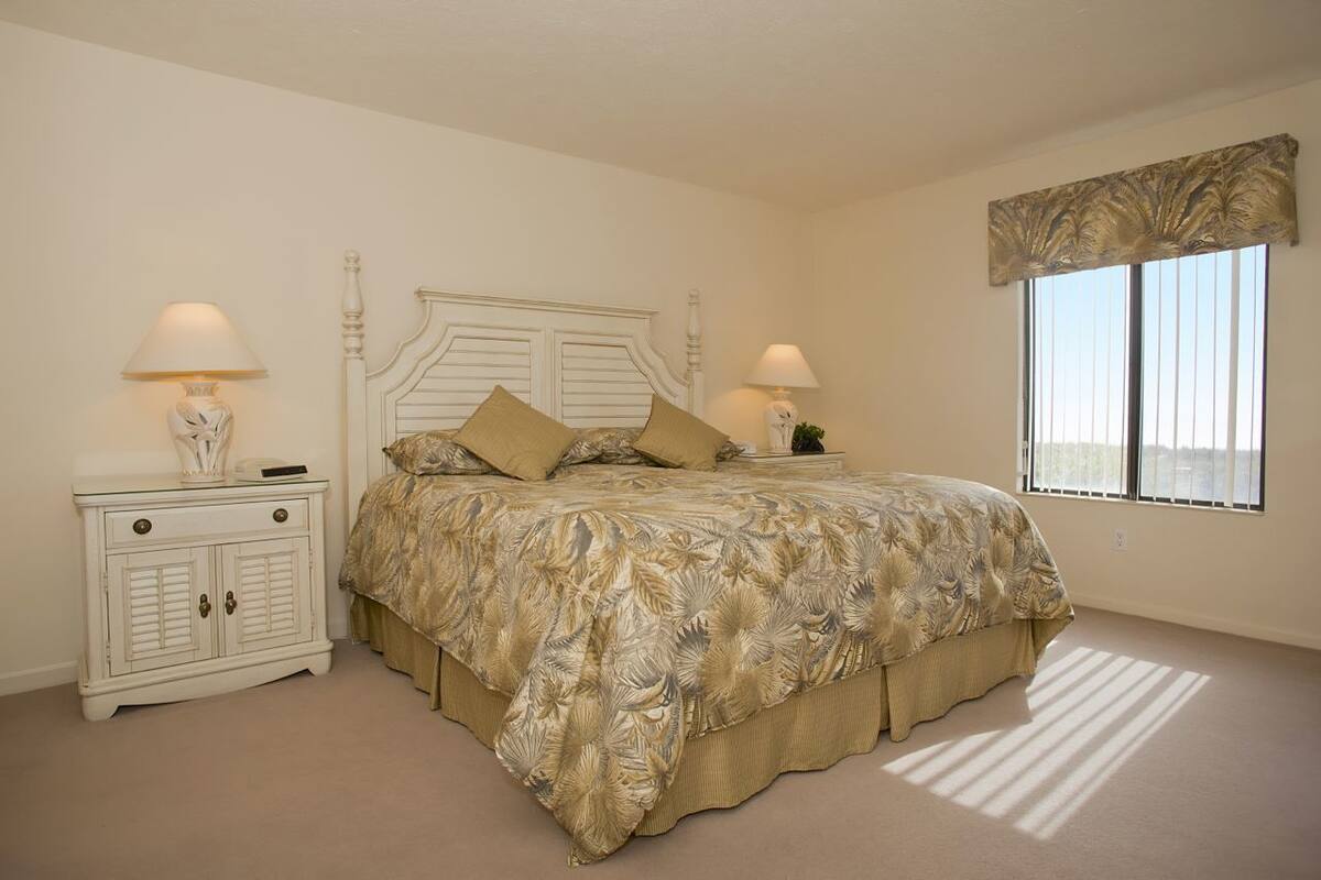 A bedroom with a bed, two nightstands, a window, and a view.