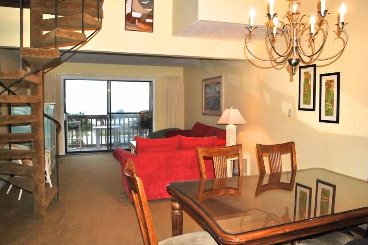 A spacious living area with a glass dining table, red sofa, and a staircase leading to an upper level.