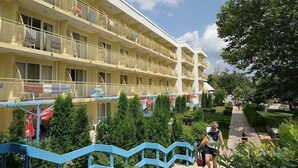 Un hotel de varios pisos con balcones, una escalera azul y una zona ajardinada.