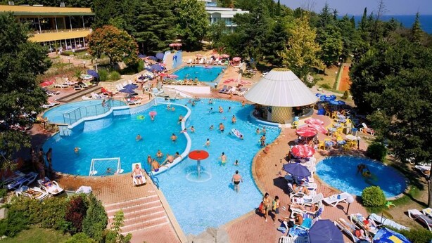 Una gran piscina al aire libre con varias secciones, rodeada de sillas de descanso y sombrillas.