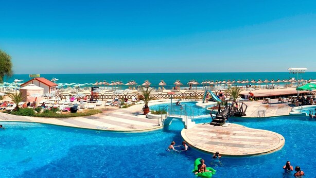 Un resort con una amplia piscina, sombrillas de playa y vistas al océano.