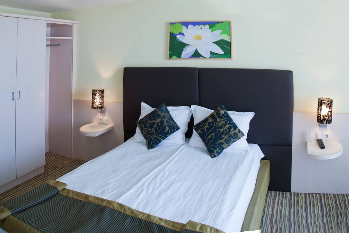 Una habitación de hotel con una cama, dos mesitas de noche, una lámpara de pared, un cuadro y un armario.