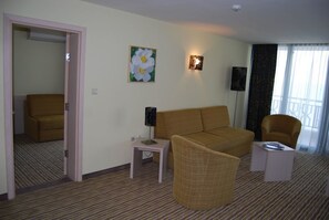 A hotel room with a sofa, armchair, and a small table with a lamp. There is a painting on the wall and a door leading to another room. - Hotel Slavuna (Kranevo)