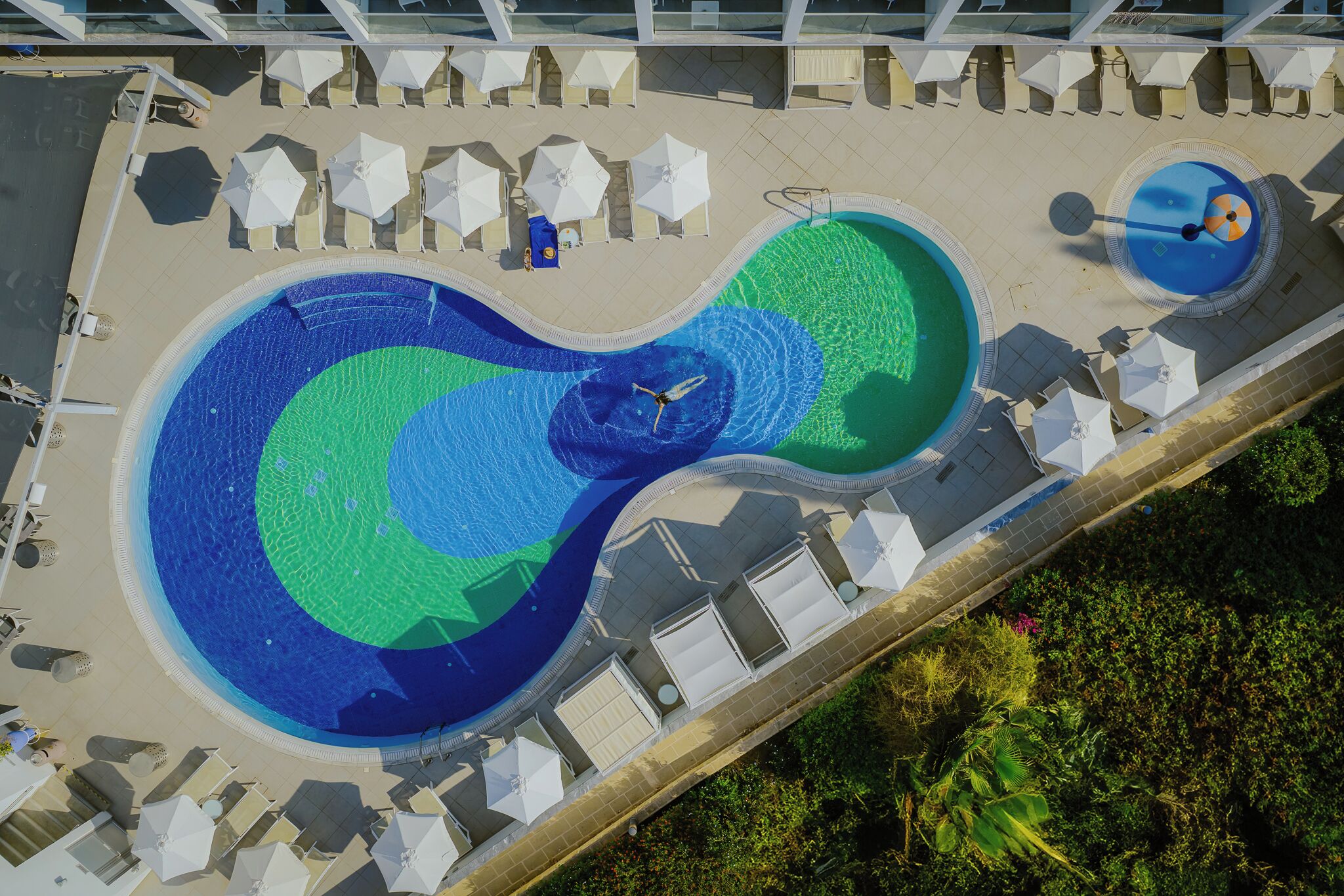 An aerial view of a pool with a unique design, surrounded by lounge chairs and umbrellas.