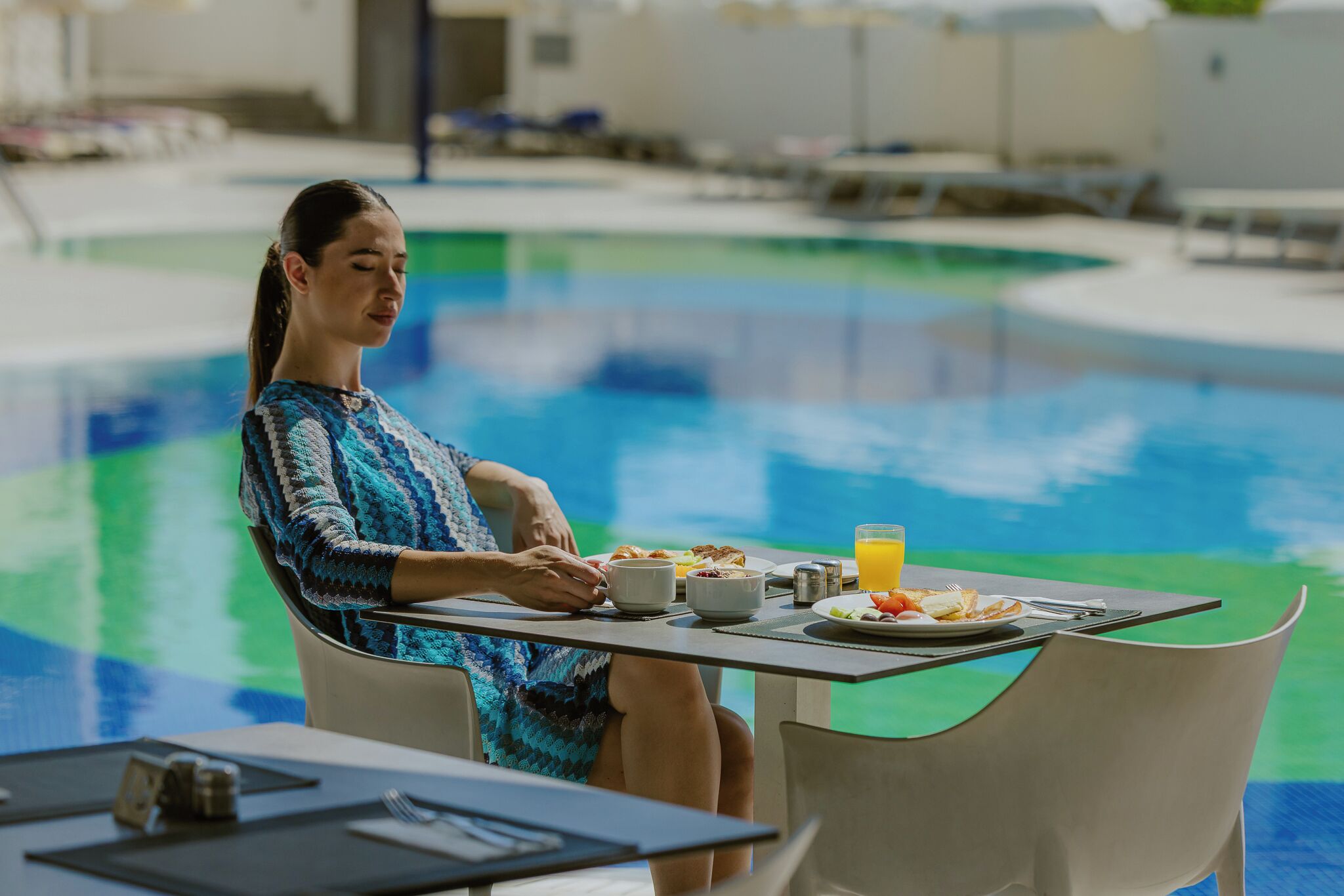 A person dining at a table by a poolside with a view of the pool.