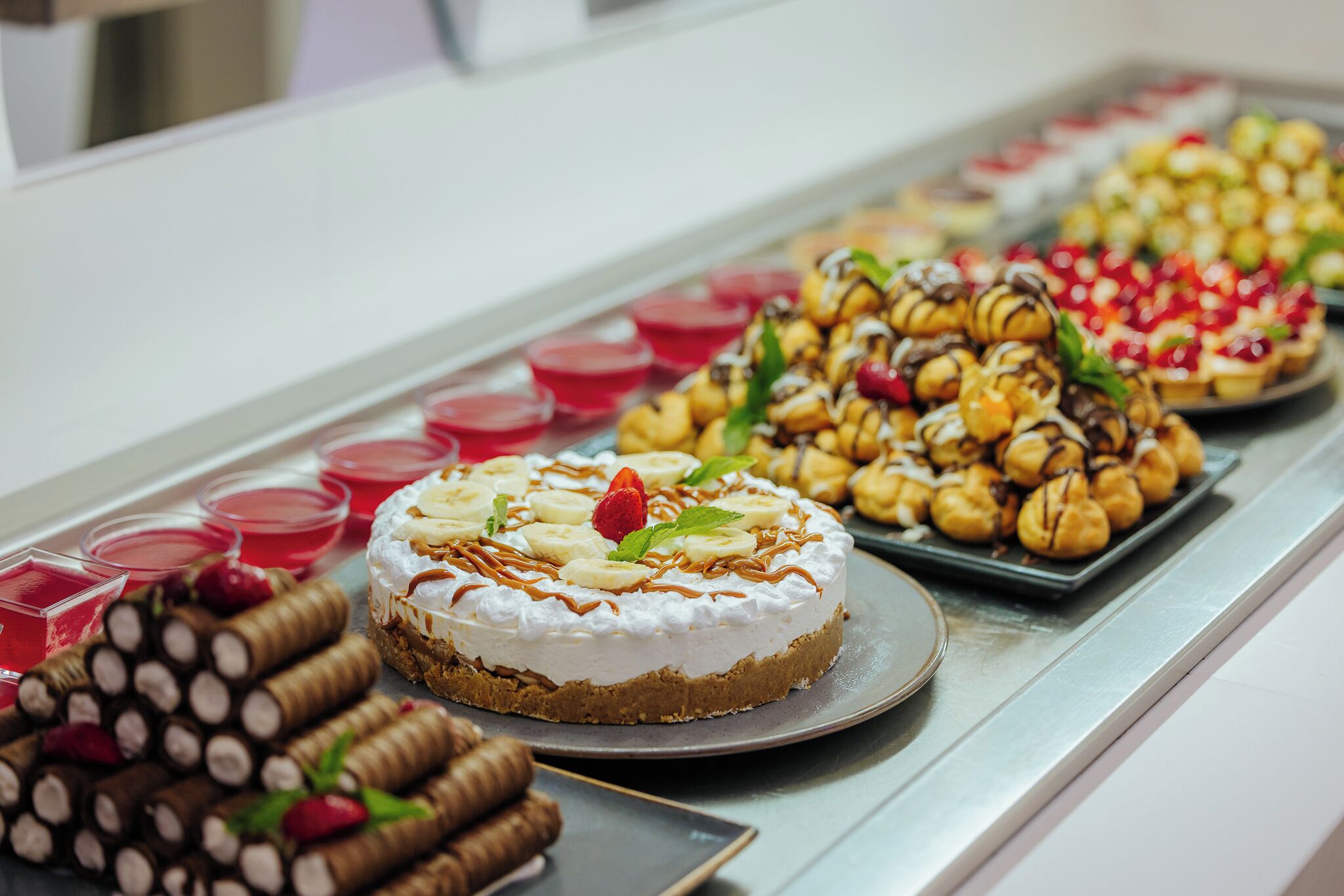A dessert display with various cakes and pastries, including a cake with whipped cream and strawberries, and chocolate-covered items.