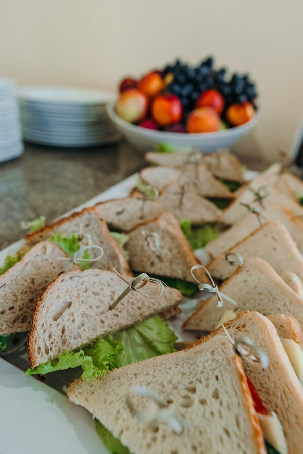 A platter of sandwiches with lettuce and cheese, a bowl of mixed fruit, and stacked plates on a table.