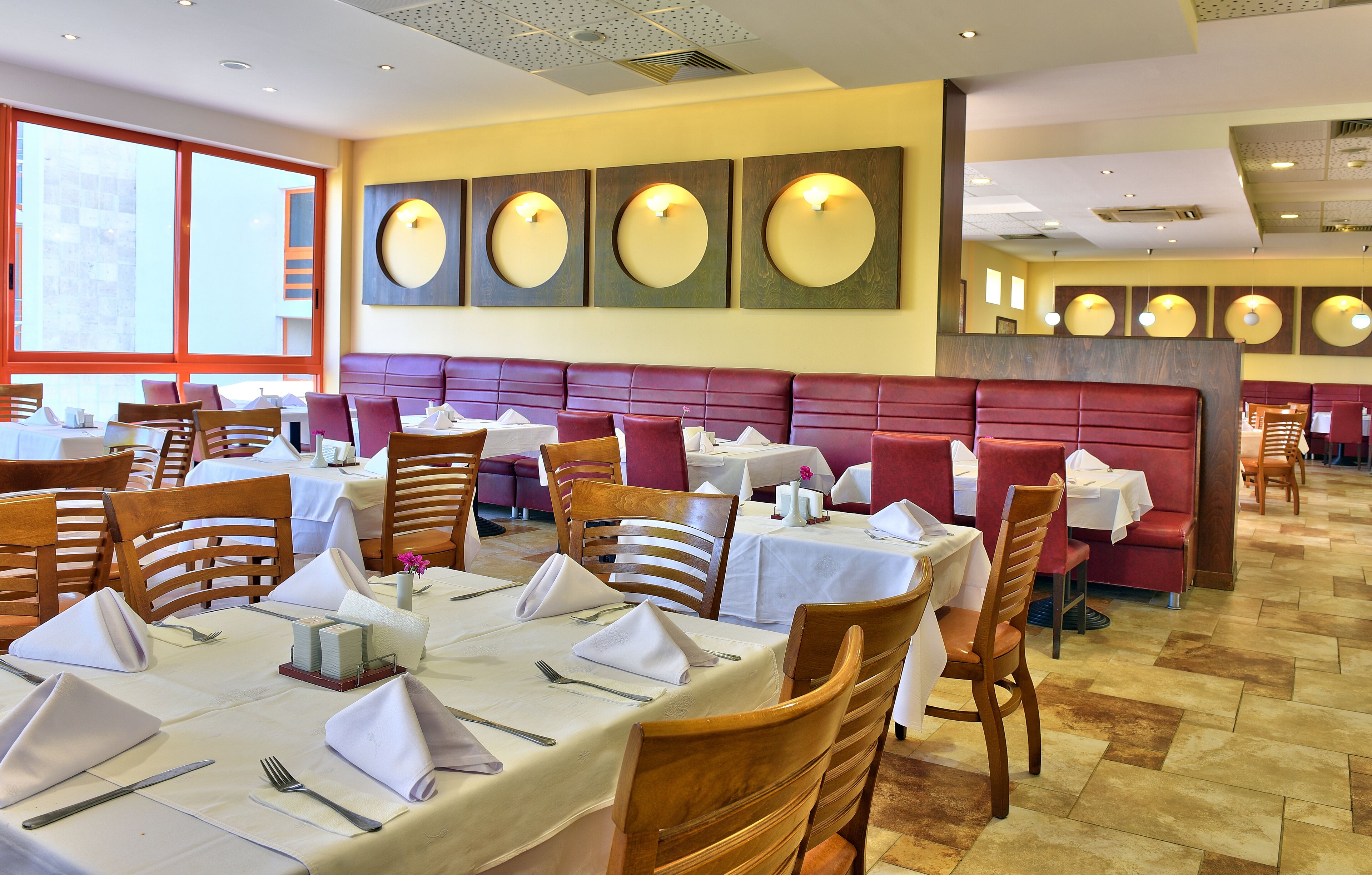 A restaurant with multiple dining tables set with white tablecloths, wooden chairs, and neatly arranged cutlery.