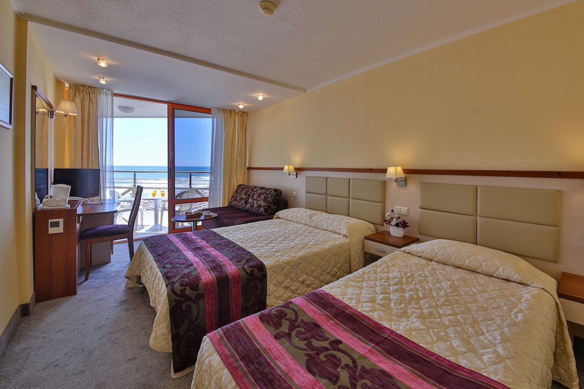 A hotel room with two beds, a desk with a computer, a chair, and a view of the beach.