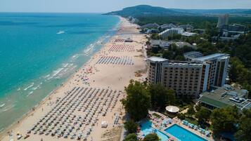 Un resort frente al mar con una amplia zona de piscina, múltiples sombrillas y una extensa playa.