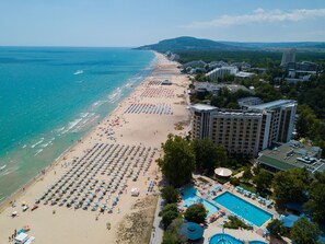 A beach resort with a large pool area, multiple beach umbrellas, and a long stretch of beach.