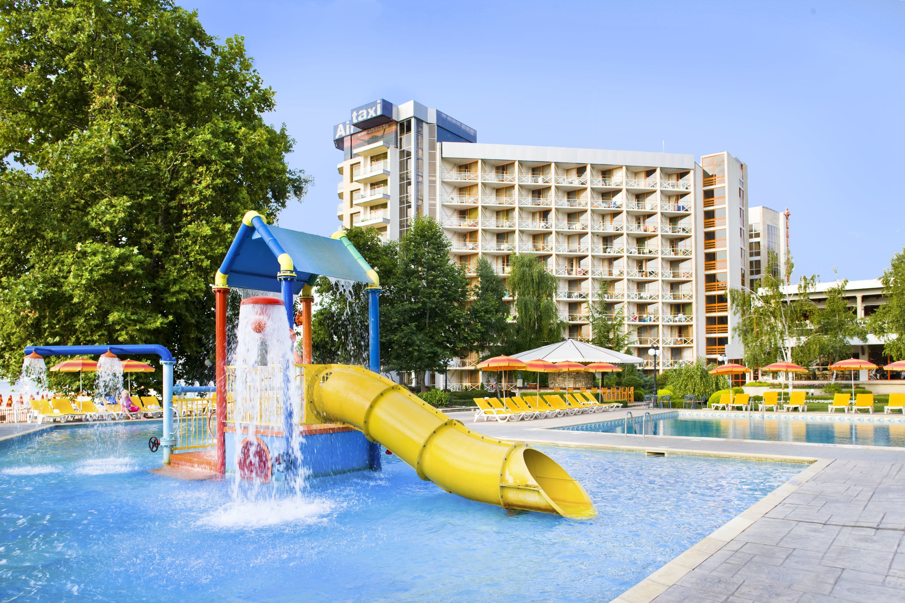 Parque acuático con un tobogán amarillo, piscina y un edificio de hotel al fondo.