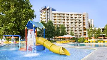 Parque acuático con un tobogán amarillo, piscina y un edificio de hotel al fondo.