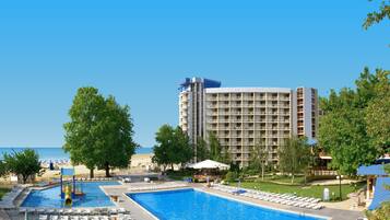 A hotel with a large swimming pool, multiple lounge areas, and a view of the sea.
