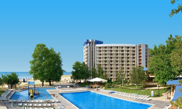 A hotel with a large swimming pool, multiple lounge areas, and a view of the sea.