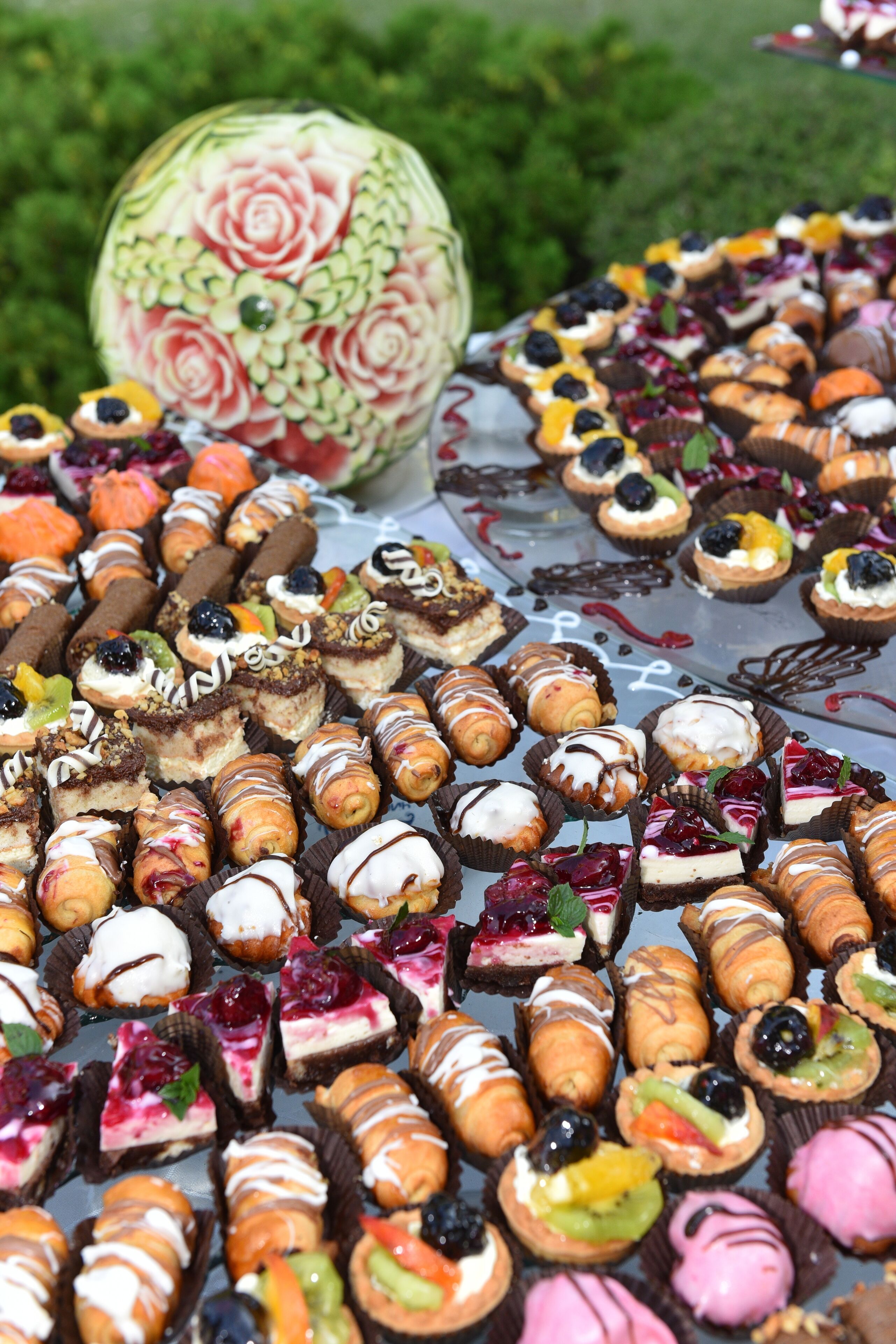 A variety of desserts arranged on a table, including cakes, pastries, and a carved watermelon.
