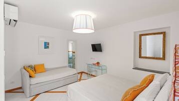 Quarto de hotel com cama, sofá, escrivaninha com cadeira, televisão e espelho.