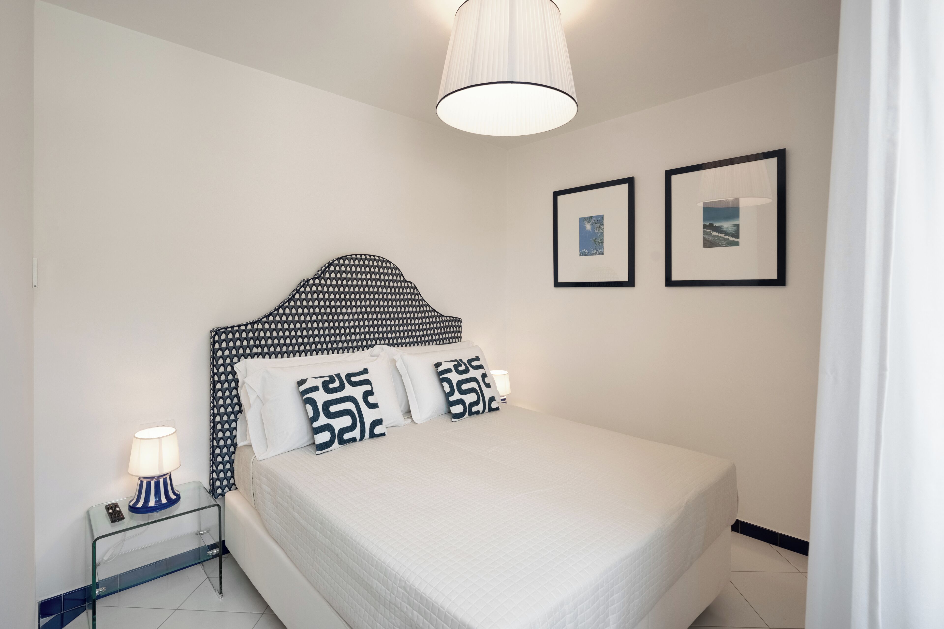 A neatly arranged bedroom with a bed, bedside table, lamp, and two framed pictures on the wall.