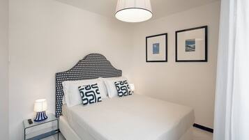 A neatly arranged bedroom with a bed, bedside table, lamp, and two framed pictures on the wall.