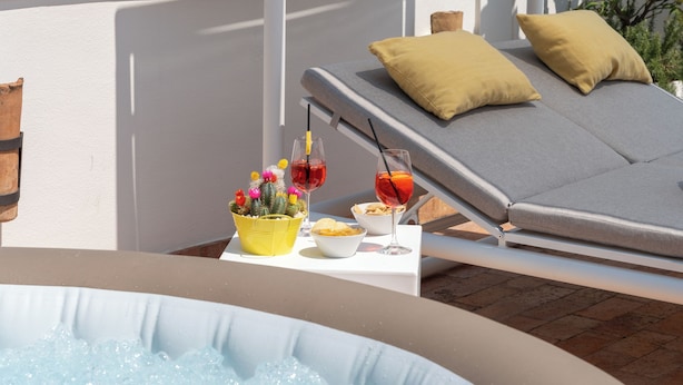 Una terraza en la azotea con jacuzzi, sillas de descanso y una mesa con bebidas y aperitivos.
